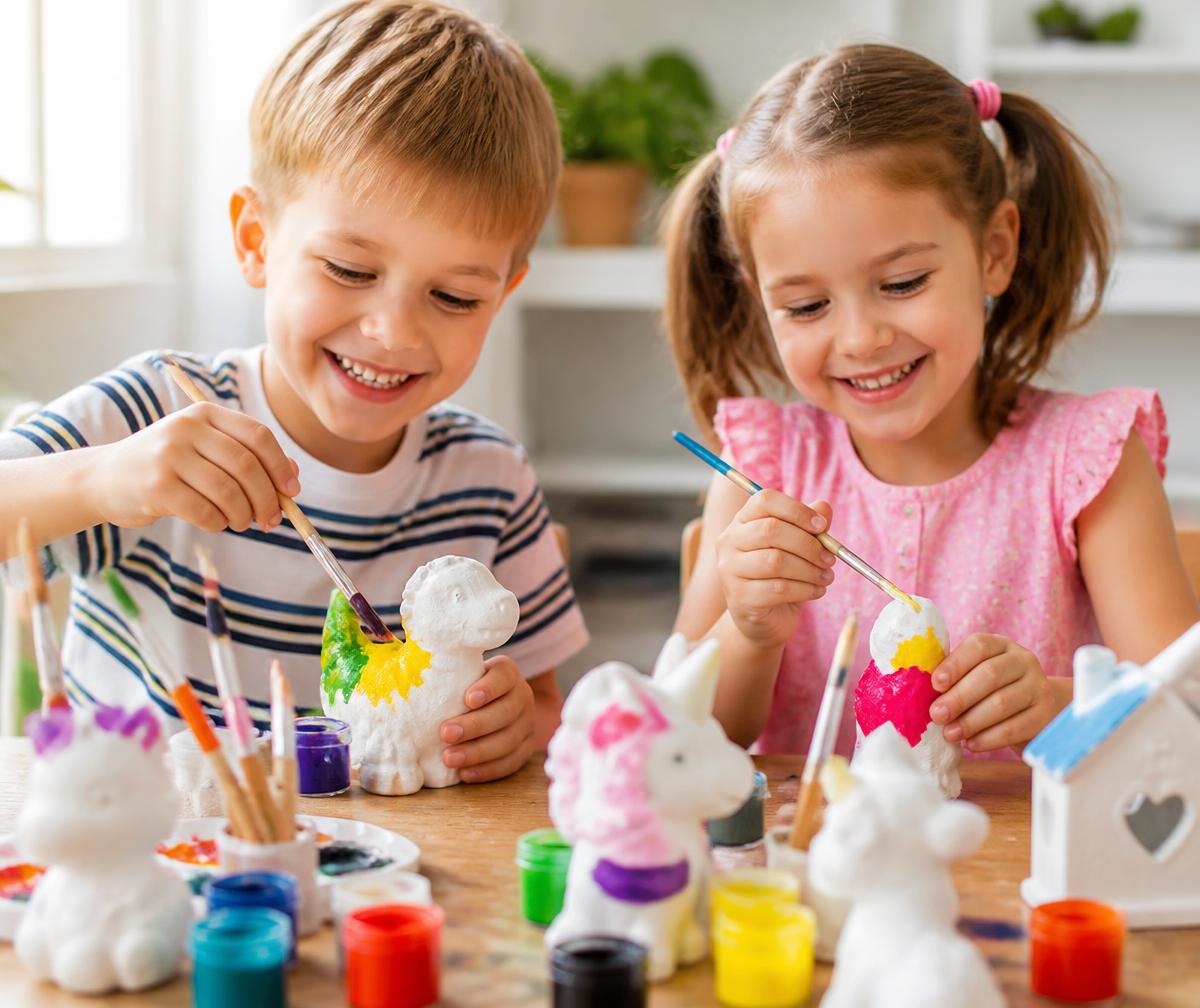 Two children painting plaster figurines at a table